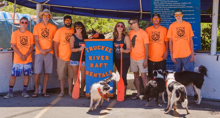 The Truckee River Raft Company crew in orange shirts with the company banner and their dogs at the Tahoe City launch site