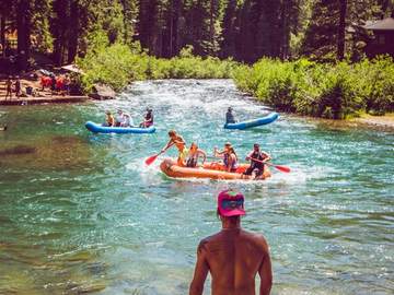 A rafter standing in the shallows as rafts pass through a riffle on the Truckee River